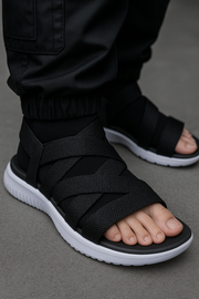 Black sandals with white soles worn by a person on a gray background