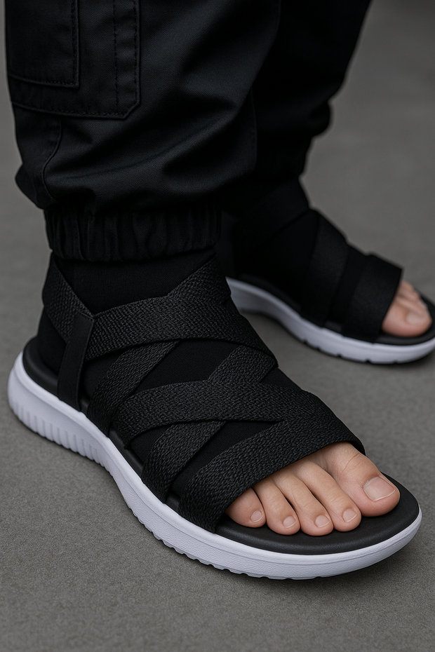 Black sandals with white soles worn by a person on a gray background
